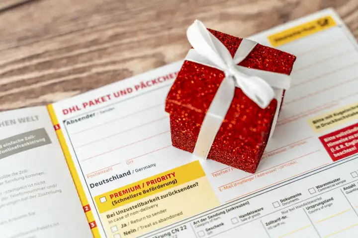 Augsburg, Bavaria, Germany - December 15, 2023: DHL Paket and Päckchen shipping label with Premium and Priority for fast delivery together with a gift for Christmas