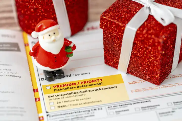 DHL Paket und Päckchen Versandschein mit Premium und Priority zur schnellen Beförderung zusammen mit einem Miniatur Weihnachtsmann und einem Geschenk zu Weihnachten