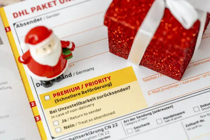 Augsburg, Bavaria, Germany - December 15, 2023: DHL parcel and small parcel shipping label with Premium and Priority for fast delivery together with a miniature Santa Claus and a gift for Christmas