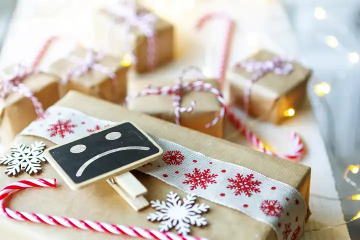 Verpackte Geschenke zu Weihnachten mit einem Schild und einem unglücklichen Gesicht. Streit und Konflikt zu den Feiertagen Konzept FOTOMONTAGE