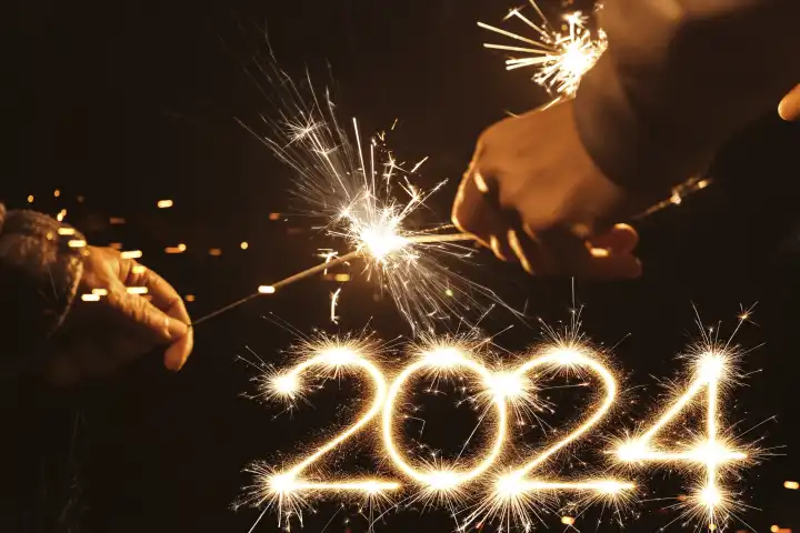 zwei Hände mit Wunderkerzen und Funken und der Jahreszahl 2024. Symbolbild Jahreswechsel Neujahr 2024 FOTOMONTAGE