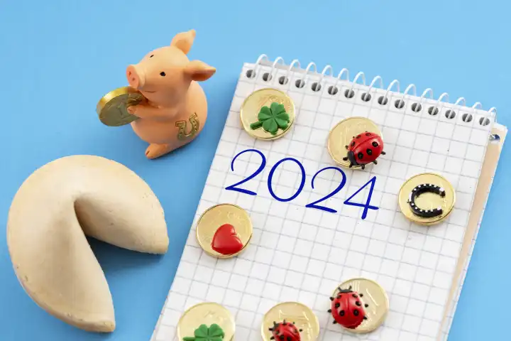 Glücksschwein und Glückskeks neben einem Schreibblock mit der Jahreszahl 2024 FOTOMONTAGE