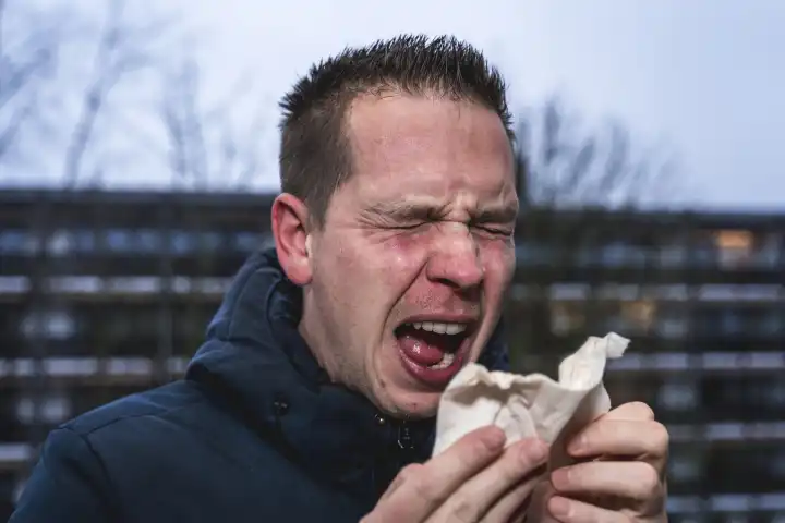 Ein kranker erkälteter Mann am Niesen mit einem Papiertaschentuch in der Hand