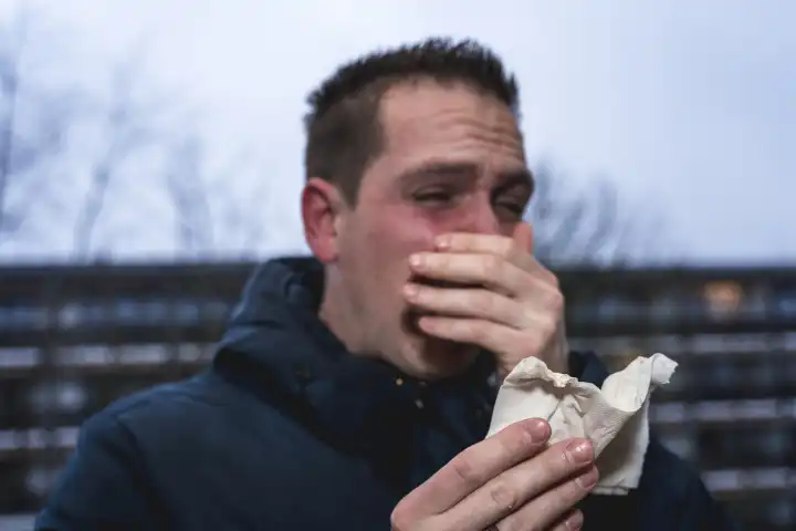 Ein kranker erkälteter Mann am Niesen mit einem Papiertaschentuch in der Hand