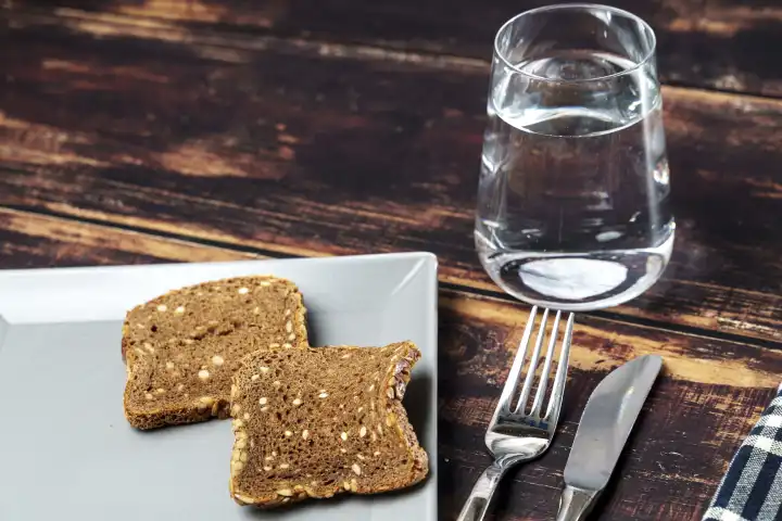 Fastenzeit Symbolbild, ein Glas Wasser neben einem Teller mit trockenen Brot