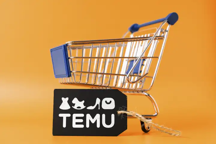 Einkaufswagen vor orangem Hintergrund mit einem Schild mit dem TEMU Logo. FOTOMONTAGE