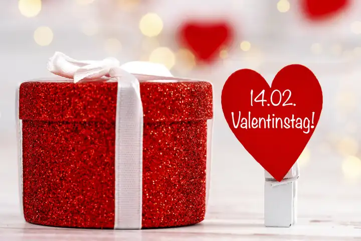 Valentinstag am 14 Februar, Schriftzug auf einem roten Herz neben einem Valentinsgeschenk FOTOMONTAGE