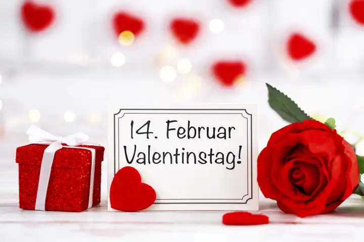 Valentinstag am 14 Februar, Schriftzug auf einer Grußkarte neben einem Geschenk und einer roten Rose FOTOMONTAGE