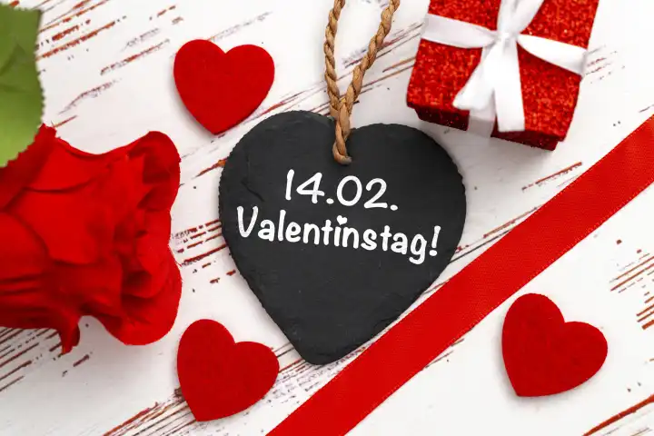 14 Februar Valentinstag, Schriftzug auf einem  Schieferherz neben einem Geschenk, roten Rosen und Herzen FOTOMONTAGE
