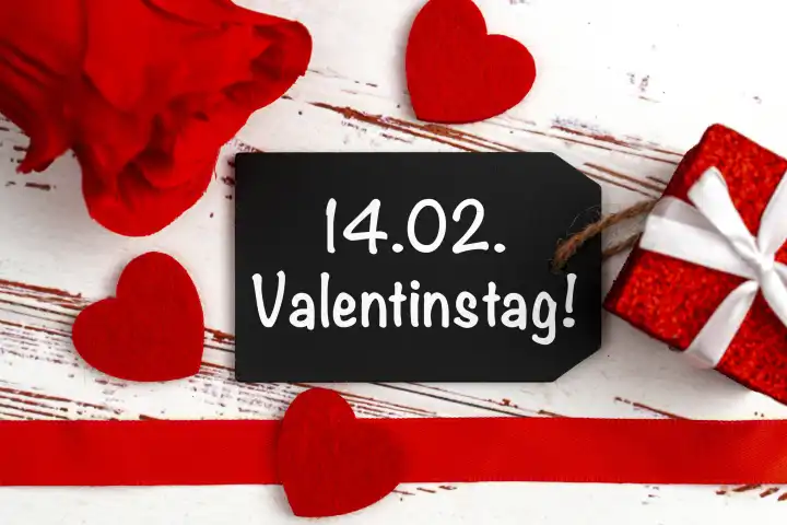 Valentinstag, 14.02. Schriftzug auf einem Geschenkanhänger neben einem Geschenk, roten Rosen und Herzen FOTOMONTAGE