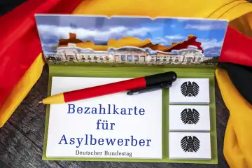 Bezahlkarte für Asylbewerber, Schriftzug auf einem Notizblock mit Bundesadler und Deutschem Bundestag abgebildet neben einer Deutschland Fahne. FOTOMONTAGE 