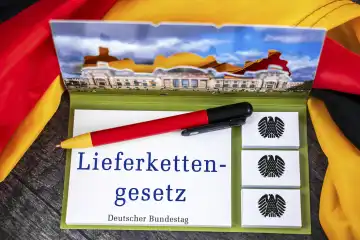 Lieferkettengesetz, Schriftzug auf einem Notizblock mit Bundesadler und Deutschem Bundestag abgebildet neben einer Deutschland Fahne. FOTOMONTAGE 