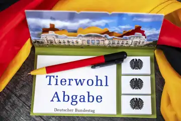 Tierwohl Abgabe, Schriftzug auf einem Notizblock mit Bundesadler und Deutschem Bundestag abgebildet neben einer Deutschland Fahne. FOTOMONTAGE 