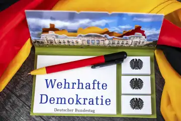 Wehrhafte Demokratie, Schriftzug auf einem Notizblock mit Bundesadler und Deutschem Bundestag abgebildet neben einer Deutschland Fahne. FOTOMONTAGE 