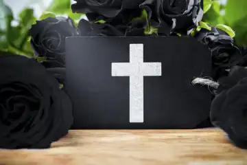 Schwarze Rosen um ein Schild mit einem Kreuz. Symbolbild Trauer und Tod. FOTOMONTAGE
