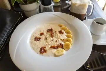 Porridge in einem Teller mit Bananen auf einem gedeckten Frühstückstisch
