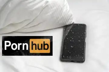 Smartphone bzw. Handy vollgeschwitz liegt auf einem Bett, neben einem Pronhub Schriftzug. Konzept Masturbation auf pornografische Inhalte, bzw. Pornos. FOTOMONTAGE