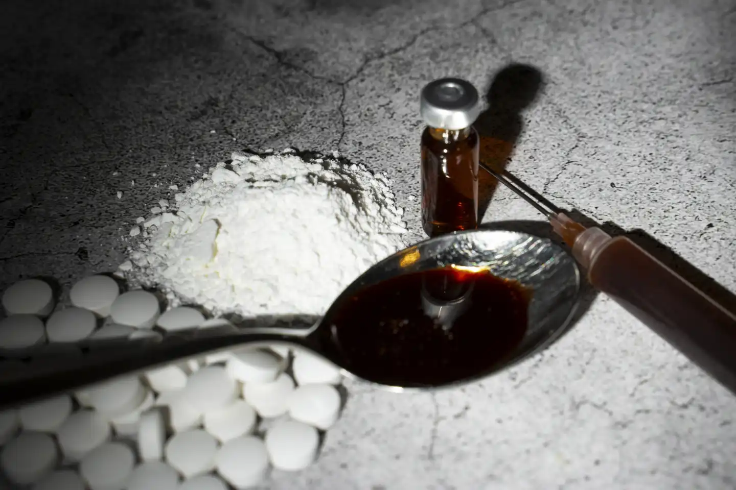 Symbolbild Drogen und illegale Substanzen. Ein Löffel mit einer braunen Flüssigkeiten neben einer Spritze, Tabletten und Pulver
