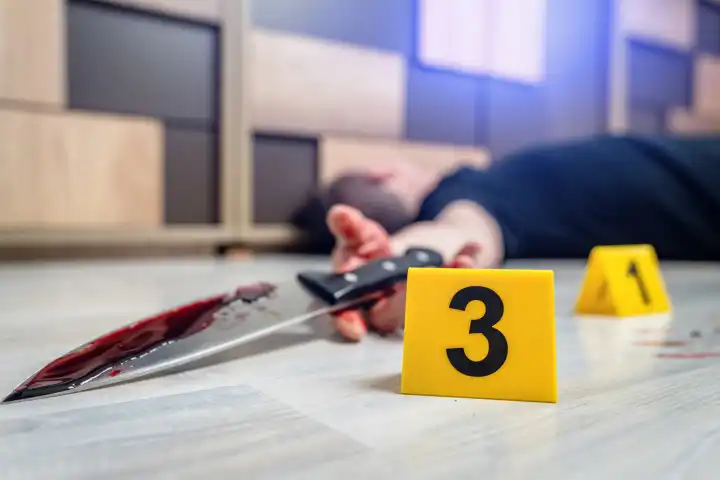  Symbolbild Tatort eines Mordfalls (gestellte Szene). Mit Blut verschmierter Mann liegt auf dem Boden mit Beweismittel Markierungen der Polizei