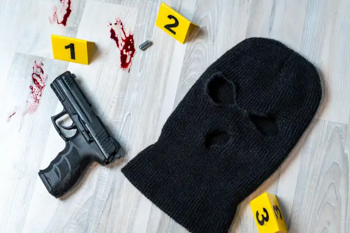 Symbolbild Überfall mit Todesfolge (gestellte Szene). Beweismittel mit Markierungen der Polizei an einem Tatort. Maskierung von einem Einbrecher, Schusswaffe und Patronenhülsen