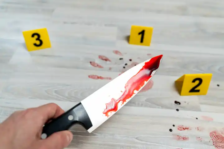 Symbolbild Messer Angriff (gestellte Szene). Ein Mann hält ein mit Blut verschmiertes Messer an einem Tatort neben Markierungen der Polizei