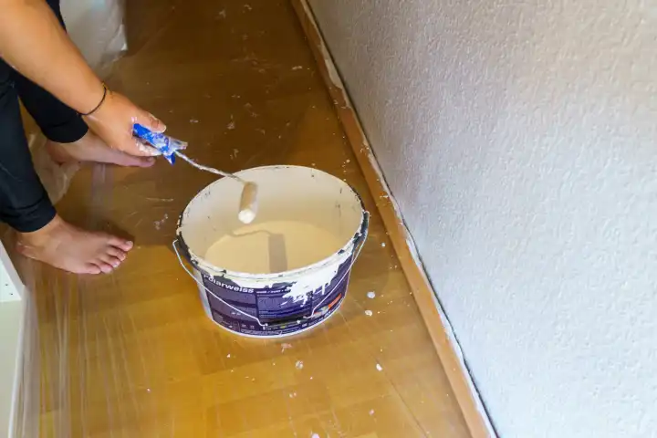 Frau streicht mit einer Farbrolle eine Wand in der Wohnung mit weißer Farbe, Polarweiß
