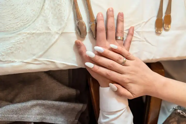 Augsburg, Bavaria, Germany - January 19, 2024: Bride and groom hold their hands with the wedding rings on each other at a festively decorated table