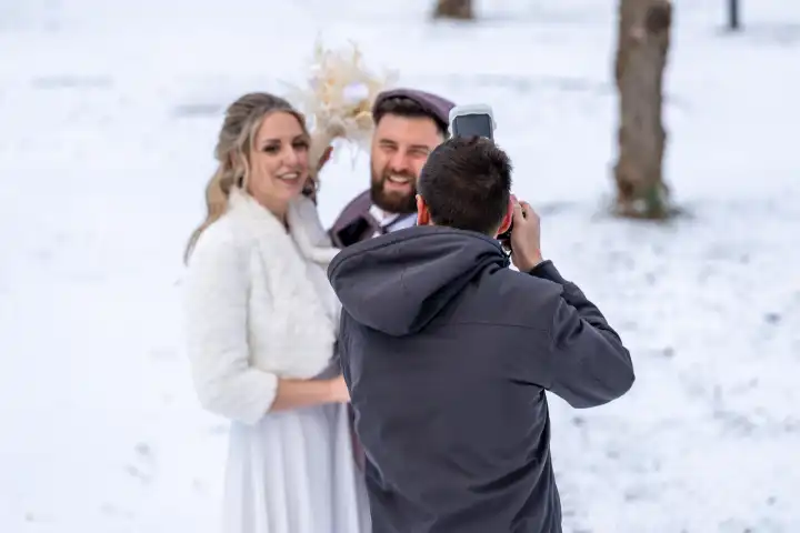 Bobingen, Bavaria, Germany - January 19, 2024: A photographer takes photos of a newlywed couple with his camera outdoors in the snow
