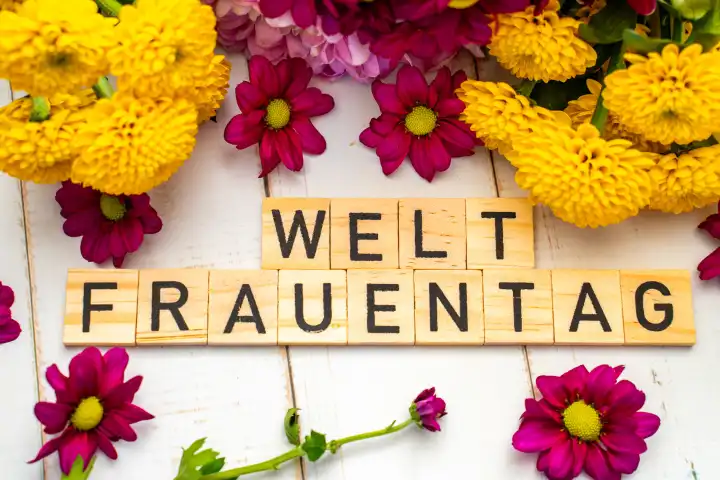 Weltfrauentag, Symbolbild am 08 März. Text: Weltfrauentag, auf Holzwürfeln neben bunten Blumen