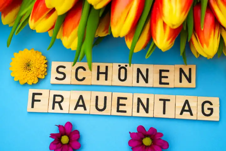 February 26, 2024: Happy Women's Day, lettering with wooden cubes on a blue background with yellow and orange tulip flowers. Symbolic image greeting for International Women's Day on March 8