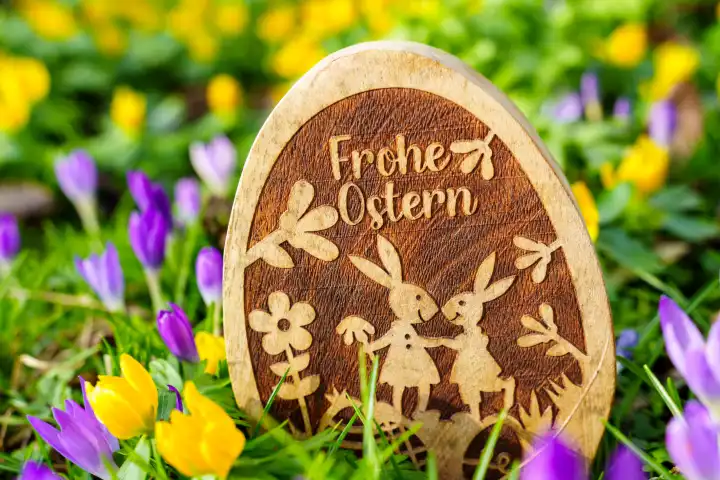 Bavaria, Germany - February 27, 2024: Happy Easter! Greeting on a wooden Easter egg standing in a meadow with spring flowers. Happy Easter lettering.