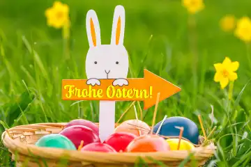 Augsburg, Bavaria, Germany - February 28, 2024: Happy Easter, greeting on a sign with an arrow held by an Easter bunny. Easter nest with colorful eggs. Greetings for Easter. PHOTOMONTAGE