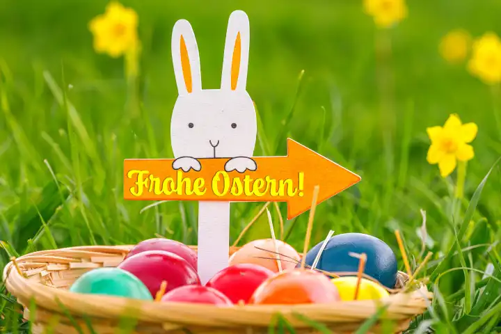 Augsburg, Bavaria, Germany - February 28, 2024: Happy Easter, greeting on a sign with an arrow held by an Easter bunny. Easter nest with colorful eggs. Greetings for Easter. PHOTOMONTAGE
