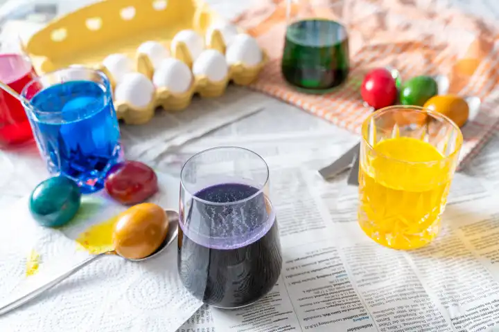 Augsburg, Bavaria, Germany - 28 February 2024: Easter egg dyeing concept, table covered with newspaper, egg dyes in jars and colorful eggs for Easter
