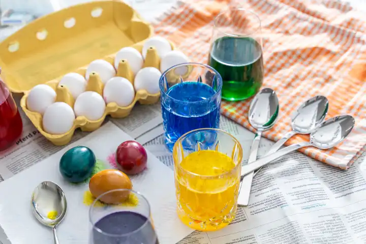 Ostereier Färben Konzept, Tisch mit Zeitung ausgelegt darauf Eierfarben in Gläsern und bunte Eier zu Ostern