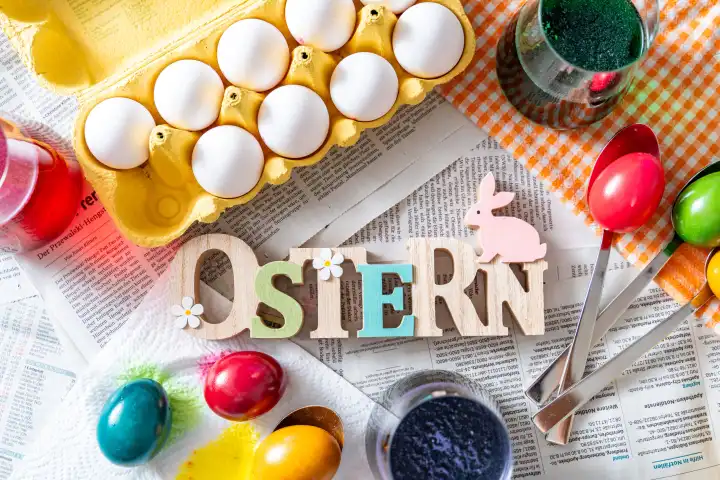 Ostern, Schriftzug aus Holz auf einem Tisch mit Zeitung ausgelegt und Zubehör zum Ostereier färben