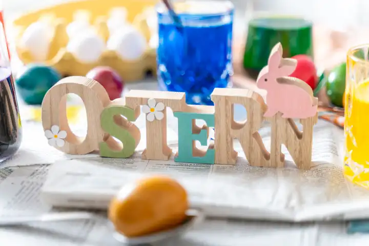 Ostern, Schriftzug aus Holz auf einem Tisch mit Zeitung ausgelegt und Zubehör zum Ostereier färben