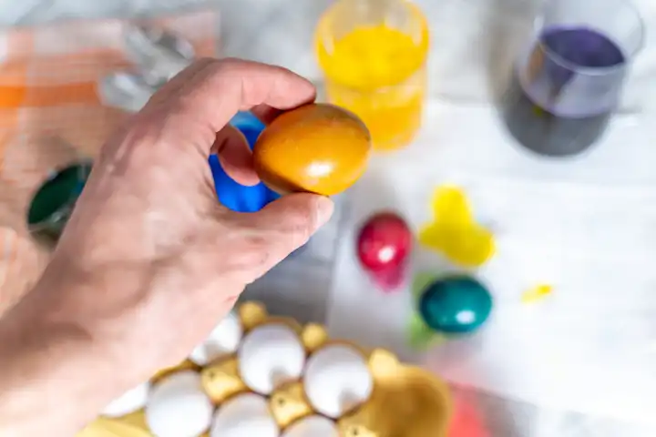 Ostereier Färben Konzept, Ein Mann hält ein gefärbtes Ei über ein Bastelset zum Eierfärben