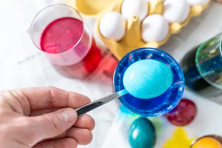 Ostereier Färben Konzept, Ein Mann färbt ein Ei in dem er es mit einem Löffel in blaue Eierfarbe hält