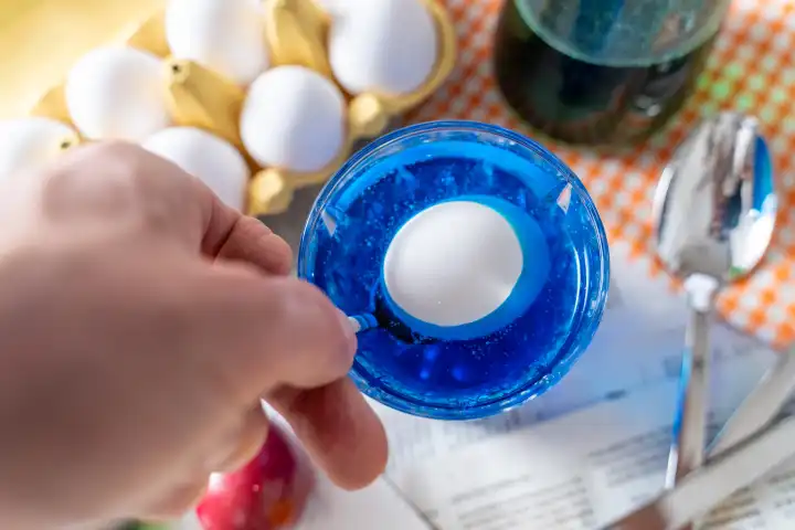 Ostereier Färben Konzept, Ein Mann färbt ein Ei in dem er es mit einem Löffel in blaue Eierfarbe hält