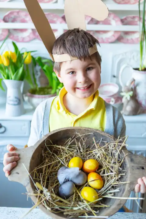 Kleiner Junge hält an Ostern ein rustikales Osternest mit Stroh und bemalten Ostereiern