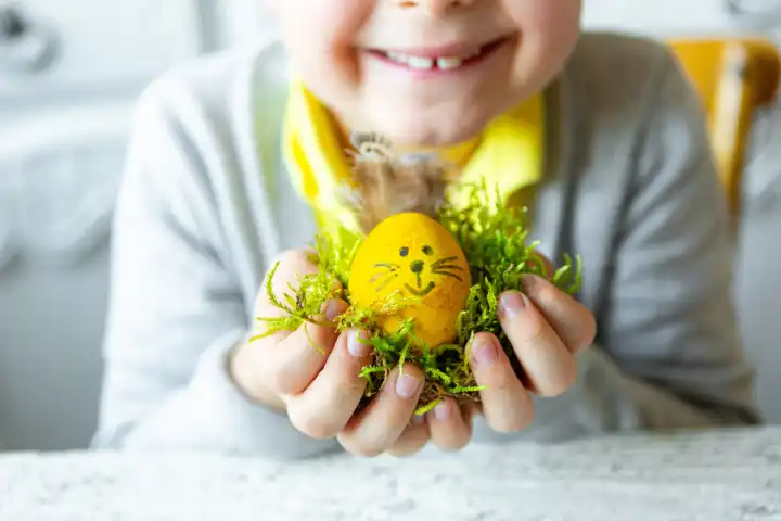 Kind hält ein selbstgebasteltes Osterei mit Hasenohren und Gesicht zu Ostern. Osternest
