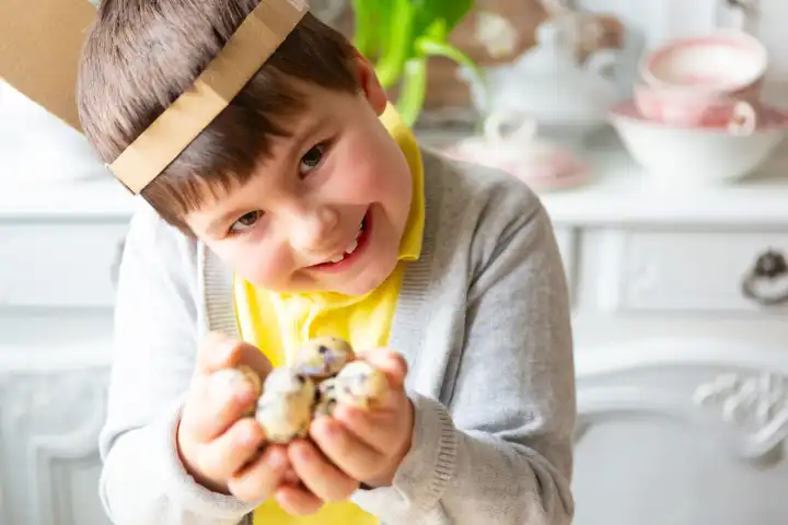 Eiersuche, Kleiner Junge hält mehrere Wachteleier zu Ostern in der Hand. Kind mit selbstgebastelten Hasenohren auf dem Kopf