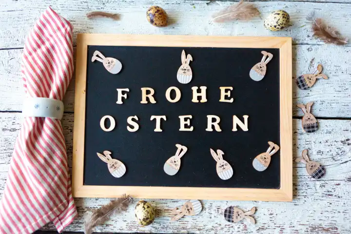 Frohe Ostern, Gruß aus Holzbuchstaben auf einer Kreidetafel mit fröhlichen Osterhasen geschmückt mit Wachteleiern