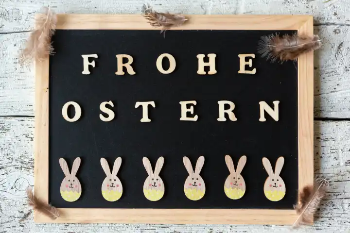Frohe Ostern, Gruß aus Holzbuchstaben auf einer Kreidetafel mit fröhlichen Osterhasen