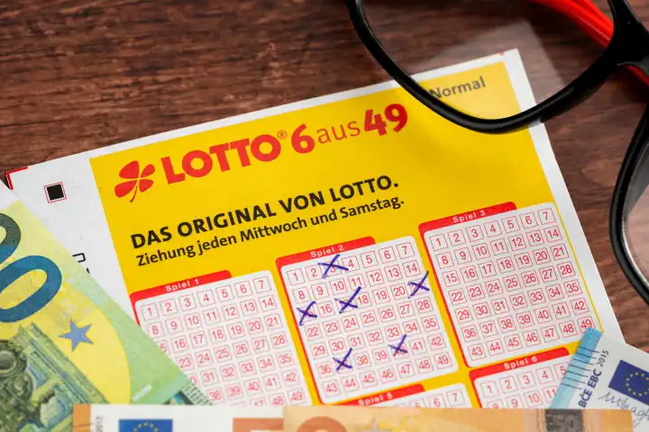Lottoschein von Lotto 6 aus 49 mit ausgefüllten Tippfeldern und Euro Geldscheinen. Glücksspiel Lotterie