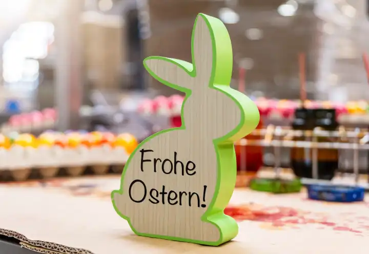 Thannhausen, Bavaria, Germany - March 10, 2024: Happy Easter, greeting on a wooden Easter bunny in an egg dyeing factory. PHOTOMONTAGE