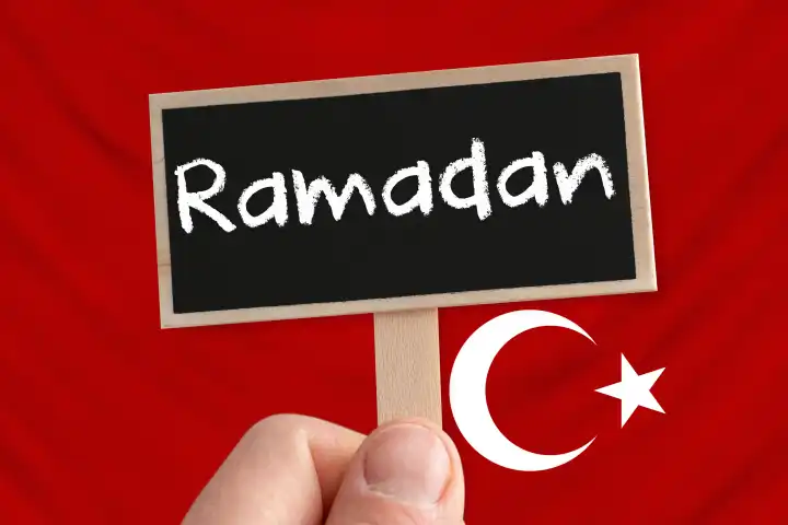 10 March 2024: Hand holding a plaque with the inscription: Ramadan in front of a Turkey flag. Ramadan is the month of fasting for Muslims. PHOTOMONTAGE