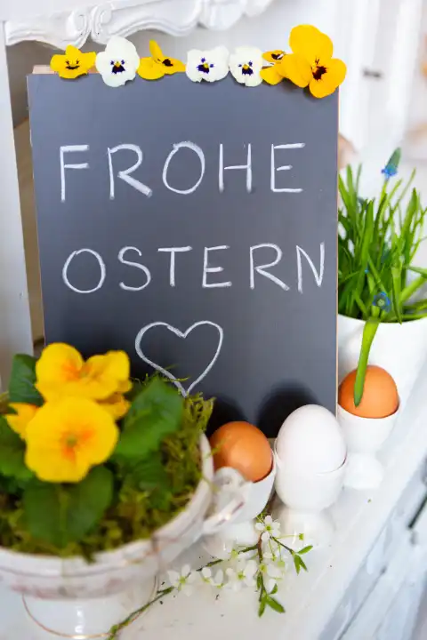 Frohe Ostern, Gruß auf einer Tafel umgeben von Dekoration zum Osterfest