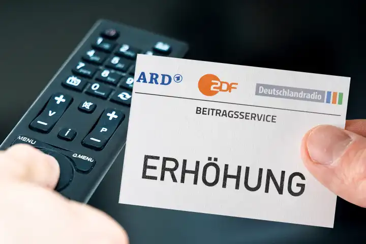 Germany - March 11, 2024: GEZ fee increase symbol image. Hand with ARD, ZDF and Deutschlandradio logo and the inscription: Increase in front of a remote control and a television. PHOTOMONTAGE